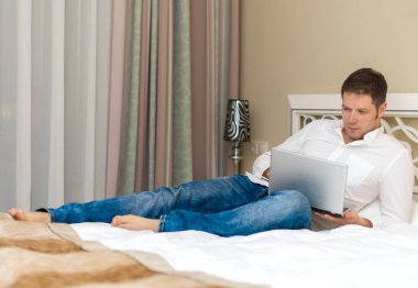 Otel odasında dizüstü bilgisayar kullanan yakışıklı adam.
