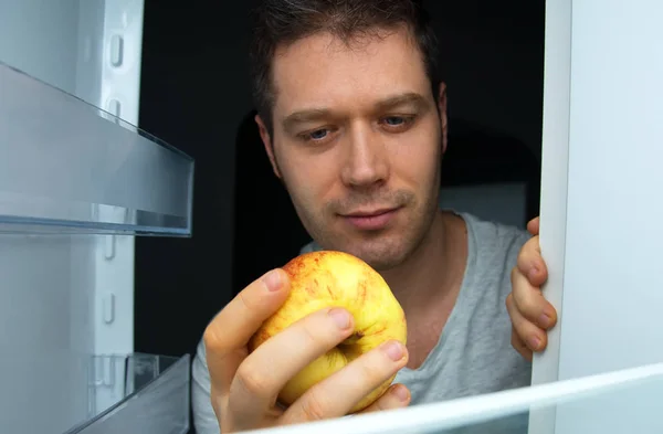 Man taking apple out of refrigerator at night. — Stock Photo, Image