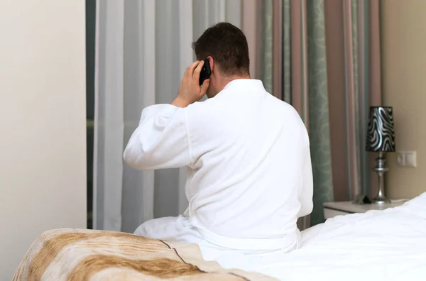 Man in badjas met mobiele telefoon in hotelkamer. — Stockfoto