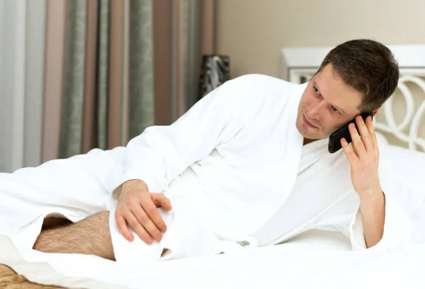 Homem de roupão de banho usando telefone celular no quarto de hotel . — Fotografia de Stock