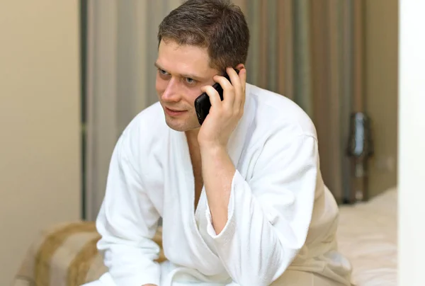 Мужчина в халате с мобильным телефоном в номере отеля . — стоковое фото