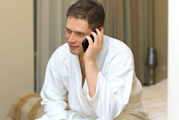 Man in badjas met mobiele telefoon in hotelkamer. — Stockfoto