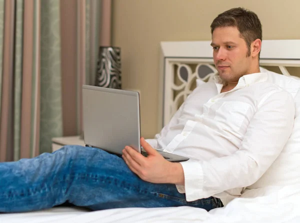 Pohledný muž používat přenosný počítač v hotelovém pokoji. — Stock fotografie