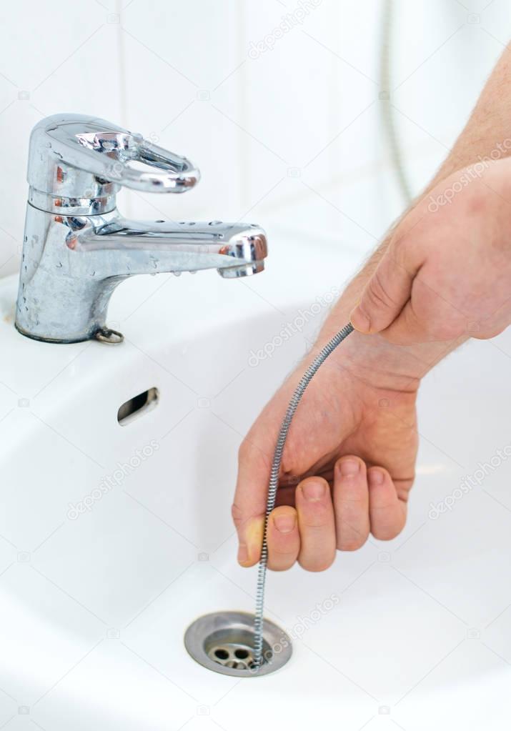 Plumber repairing sink with plumber's snake.