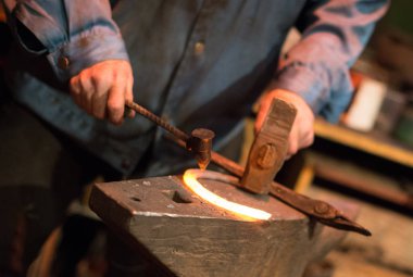 At nalı yapımında. At nalı çivi delikleri yapma çekiç ile erkek işçi.