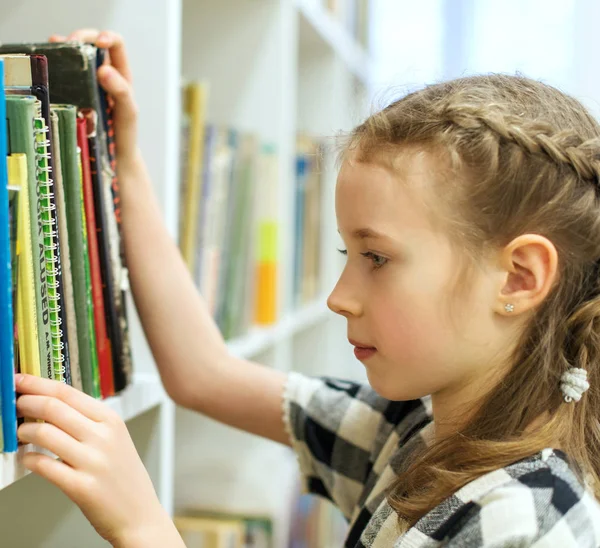 Menina bonita à procura de um livro na biblioteca . — Fotografia de Stock