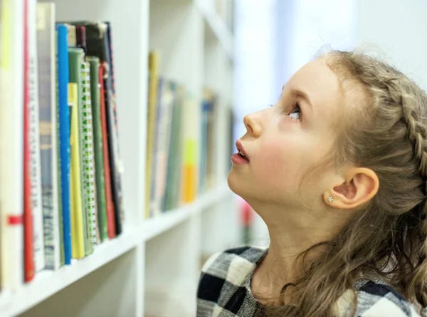 Menina bonita à procura de um livro na biblioteca . — Fotografia de Stock