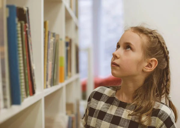 Красивая маленькая девочка ищет книгу в библиотеке . — стоковое фото
