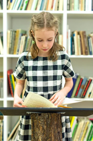 Mooi klein meisje het lezen van een boek in de bibliotheek. — Stockfoto