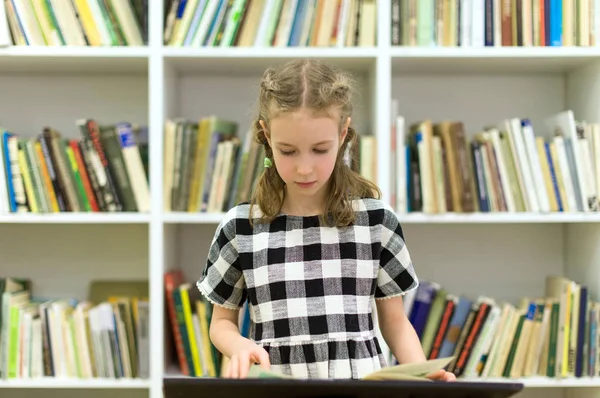 Całkiem mała dziewczynka z książką w bibliotece. — Zdjęcie stockowe