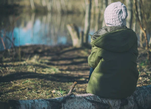 Kleines Mädchen sitzt auf einem Baumstamm im Wald. — Stockfoto