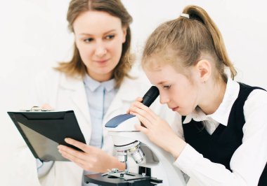 Kadın ve küçük kızı laboratuarda mikroskop kullanarak.