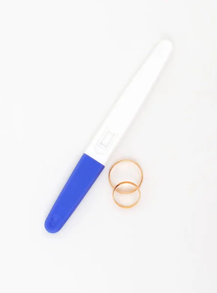 Teste de gravidez de plástico e dois anéis de casamento na mesa . — Fotografia de Stock
