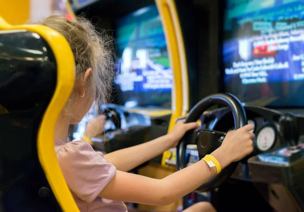 小さな女の子がレースゲーム シミュレータ テーマパークで遊んで. — ストック写真