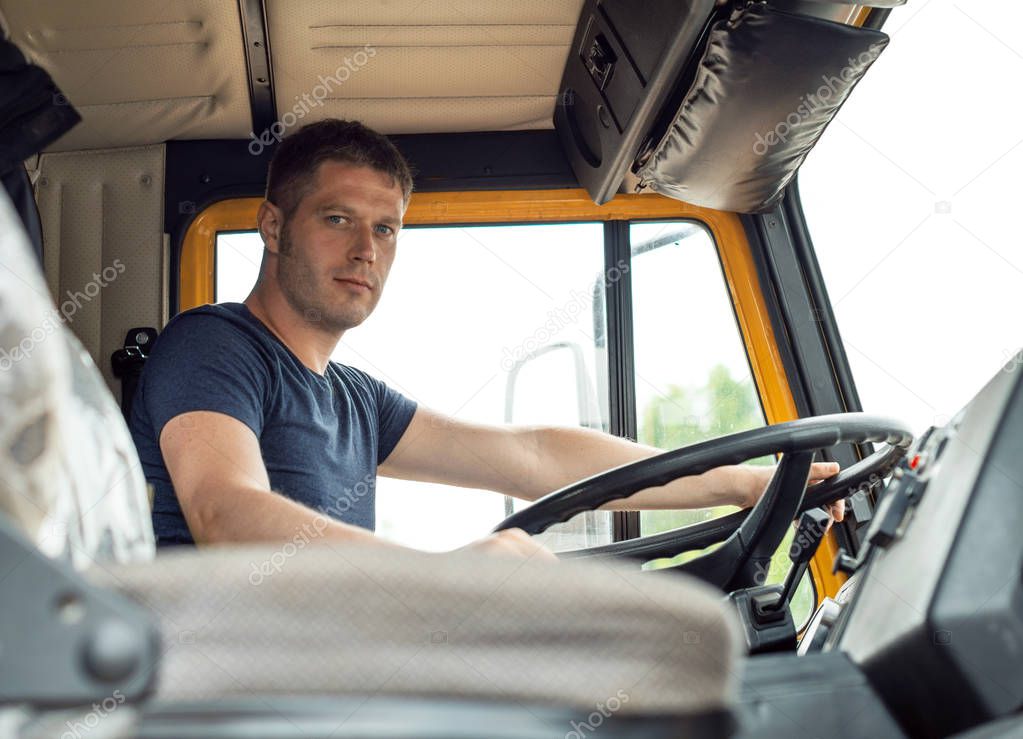 Male trucker in cabin of his yellow truck.