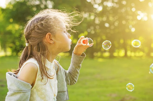 Klein meisje blazen zeepbellen in het park. — Stockfoto