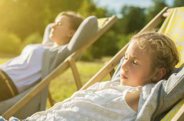 Kvinna och hennes dotter njuter solen i schäslong. — Stockfoto