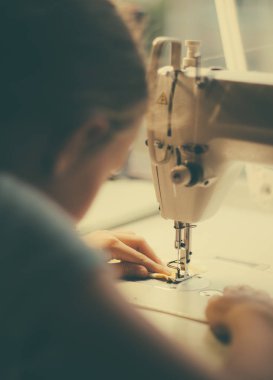 Küçük kız evde dikiş makinesi üzerinde çalışıyor. Yakın çekim görünümü.