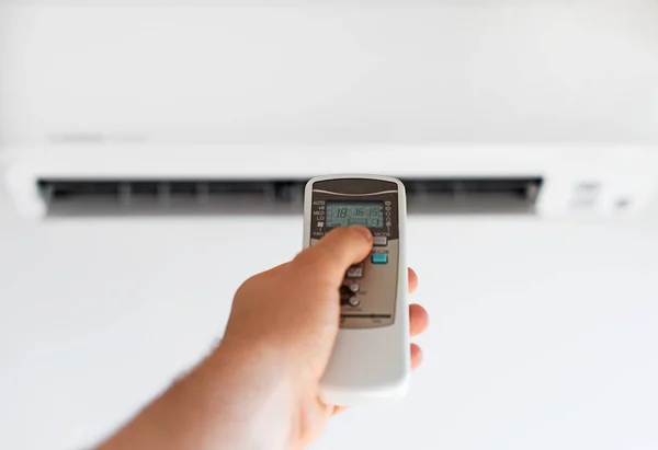 Hand holding remote control aimed at the air conditioner. — Stock Photo, Image