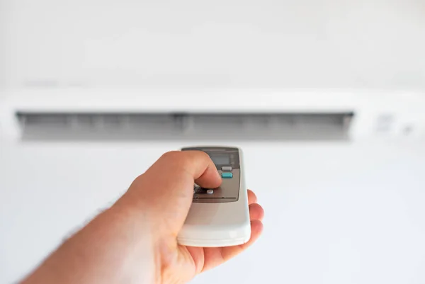 Hand met afstandsbediening gericht op de air conditioner. — Stockfoto