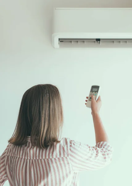 Mujer sosteniendo control remoto dirigido al aire acondicionado . — Foto de Stock