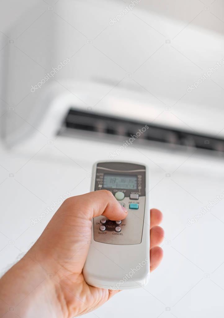 Hand holding remote control aimed at the air conditioner.