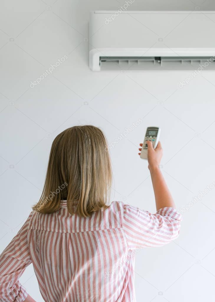 Woman holding remote control aimed at the air conditioner.