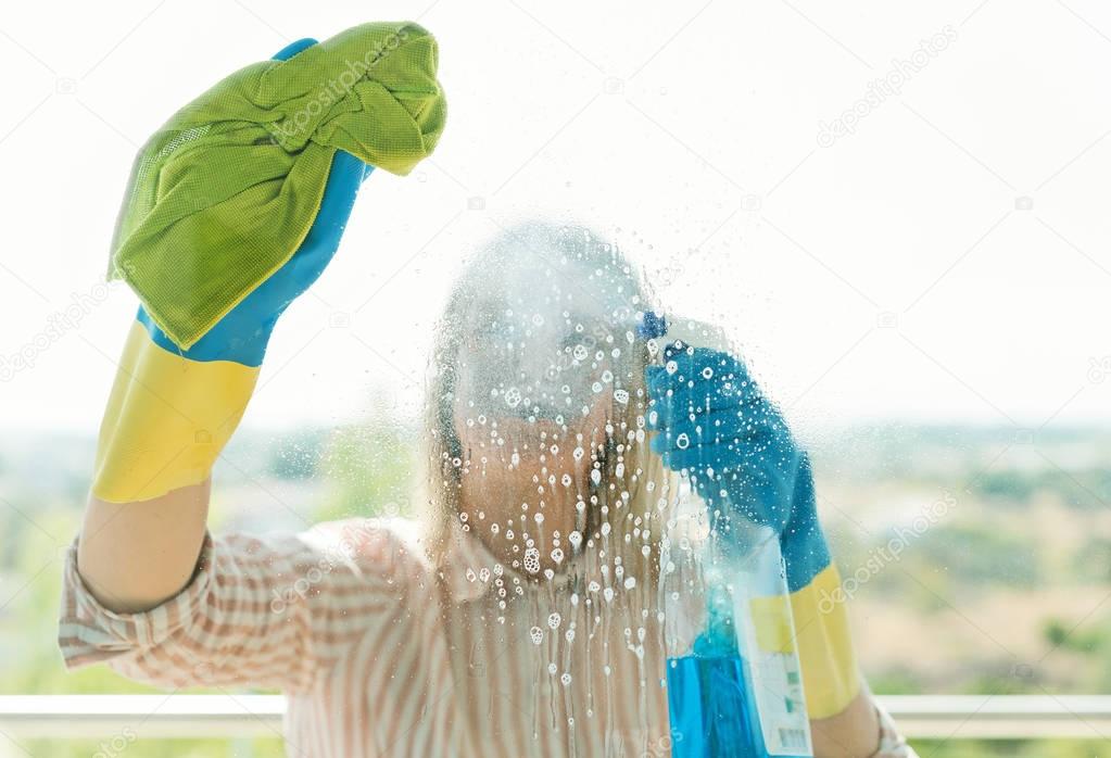 House cleaning. Woman is wiping glass on the balcony.