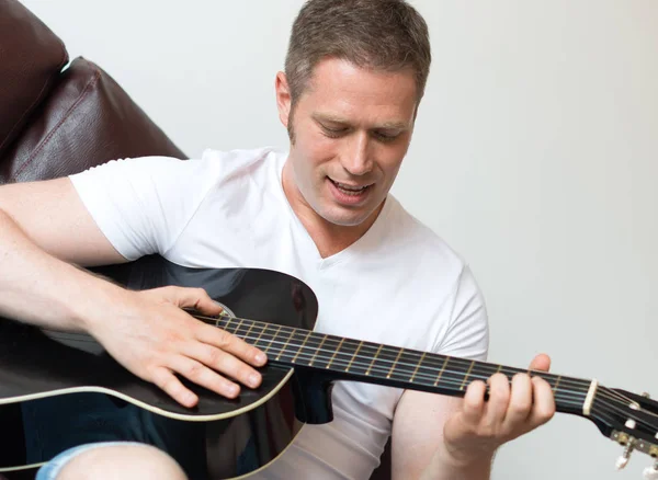 Pohledný muž hraje doma na kytaru. — Stock fotografie