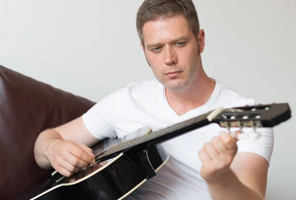 Hombre guapo afinando una guitarra en casa . — Foto de Stock