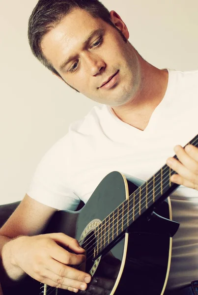 Pohledný muž hraje doma na kytaru. — Stock fotografie