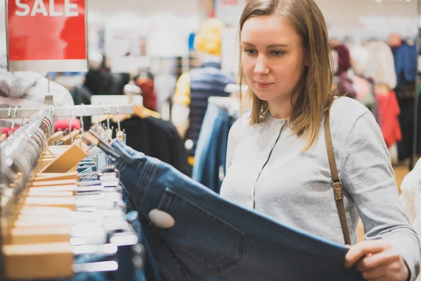 Vrouw kiezen jeans in kledingwinkel. — Stockfoto
