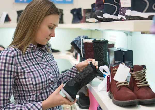 Mooie vrouw kiezen kinderen winter laarzen in het winkelcentrum. — Stockfoto