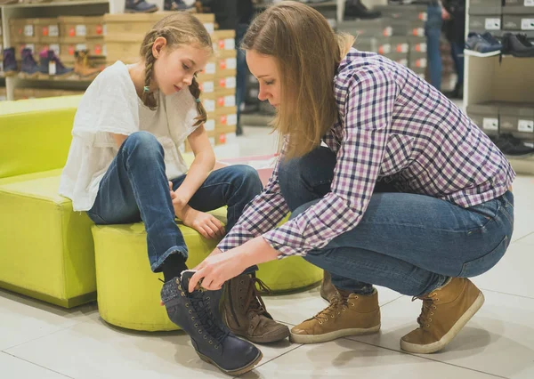 Moeder kiest winter schoenen voor haar dochter in de winkel. — Stockfoto