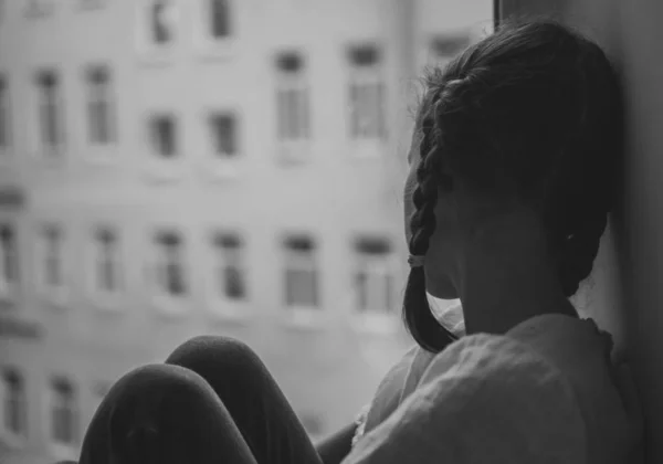 Niña triste sentada cerca de la ventana. Blanco y negro . —  Fotos de Stock