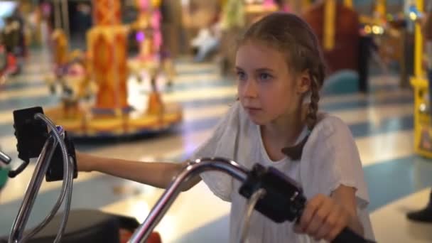 小さな女の子がテーマパークでバイクのシミュレーターのゲームを遊んで — ストック動画