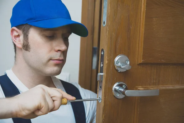 Young handyman in uniform changing door lock. — Stock Photo, Image