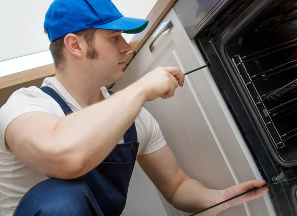 Professionele klusjesman in overalls herstellen van binnenlandse oven in de keuken. — Stockfoto