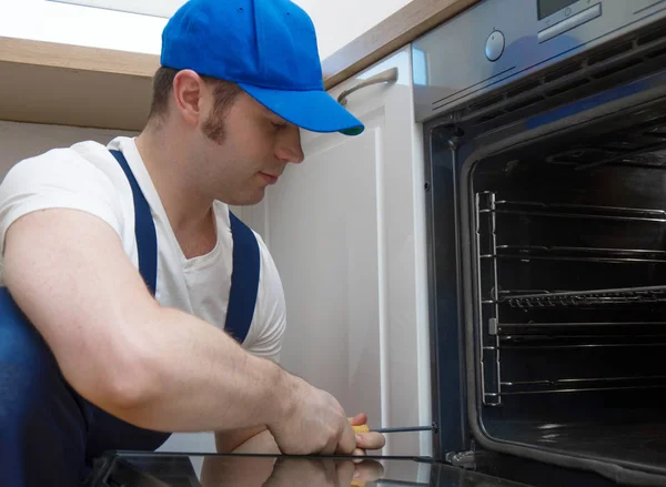 Professional handyman in overalls repairing domestic oven in the kitchen. — Stock Photo, Image