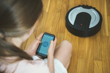 Robot elektrikli süpürge denetlemek için mobil uygulaması kullanan küçük kız.