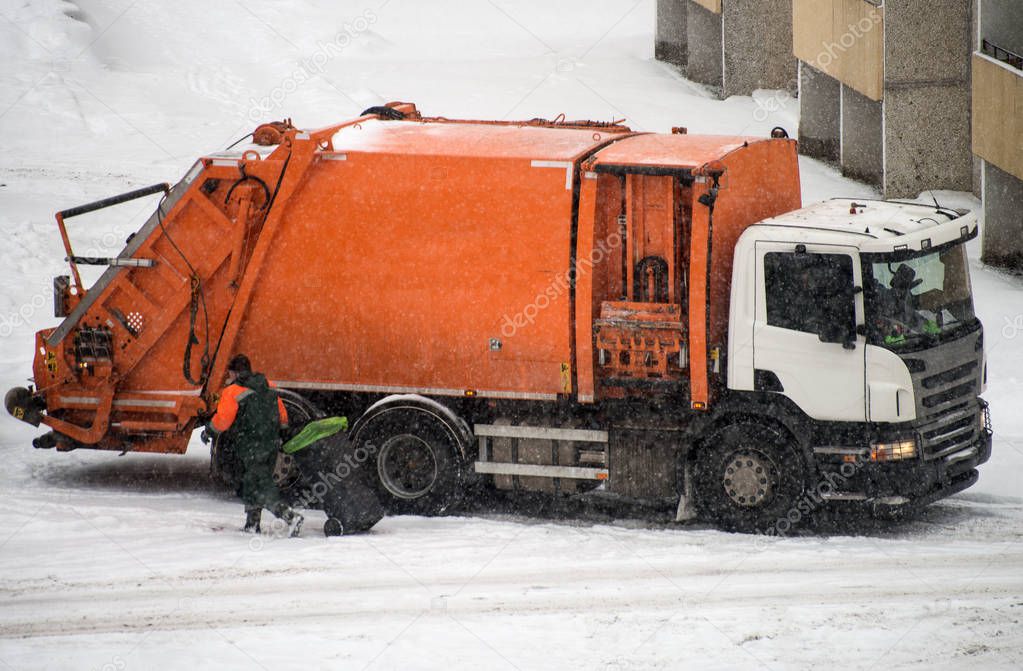 Garbage truck takes away garbage in snowy weather.