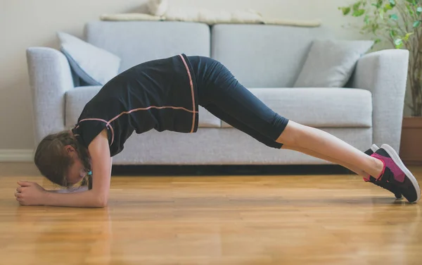 Liten flicka gör övningar för abs hemma. Plankan. — Stockfoto