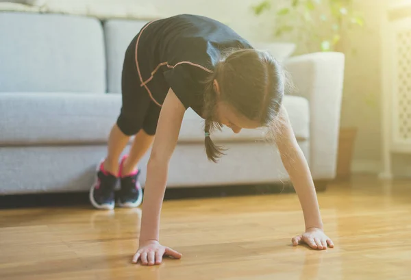 Mała dziewczynka robi push up w domu. Gimnastyka w domu. — Zdjęcie stockowe