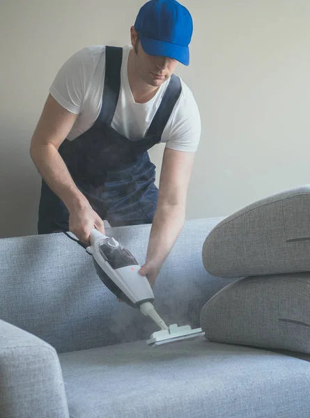 Чоловік в уніформі чистки тканини дивана з сухим пароочищувачем . — стокове фото