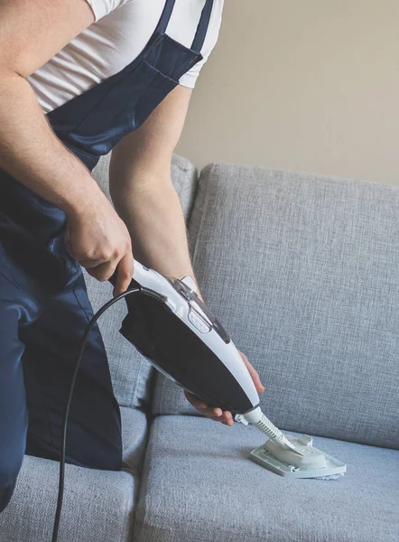 Homme en tissu de nettoyage uniforme du canapé avec nettoyeur à vapeur sèche . — Photo