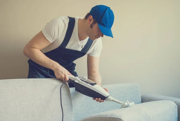Férfi takarítás kanapé száraz gőzzel tisztító egyenruhában. Hely a szöveg. — Stock Fotó
