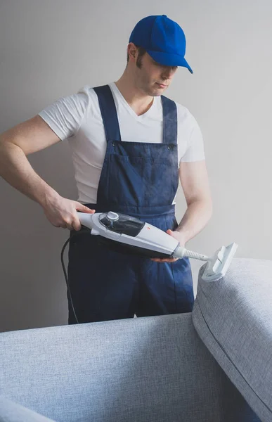 Homem em tecido de limpeza uniforme do sofá com aspirador de vapor seco . — Fotografia de Stock