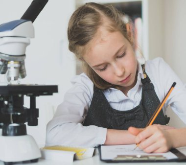 Küçük kız masada mikroskop ile fen bilgisi dersinde.