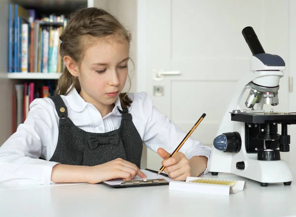 Petite fille en classe de sciences avec microscope sur la table . — Photo
