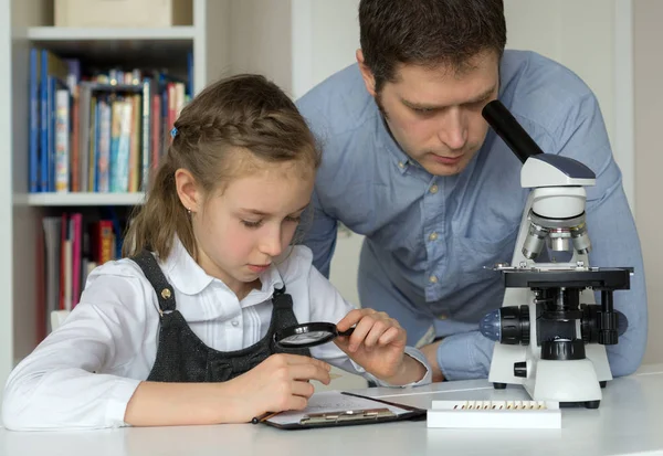 Маленькая девочка с учителем в классе естественных наук с микроскопом на столе . — стоковое фото